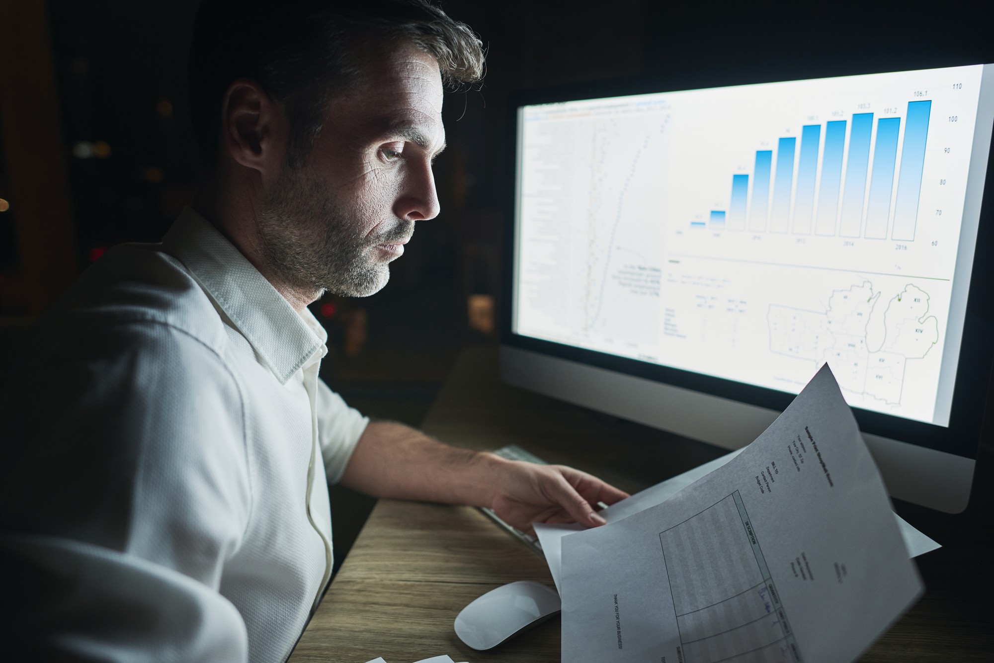 Professional man analyzing documents at his desk with data charts and graphs on a computer screen, representing data driven mortgage rate strategies and data-driven decision-making.