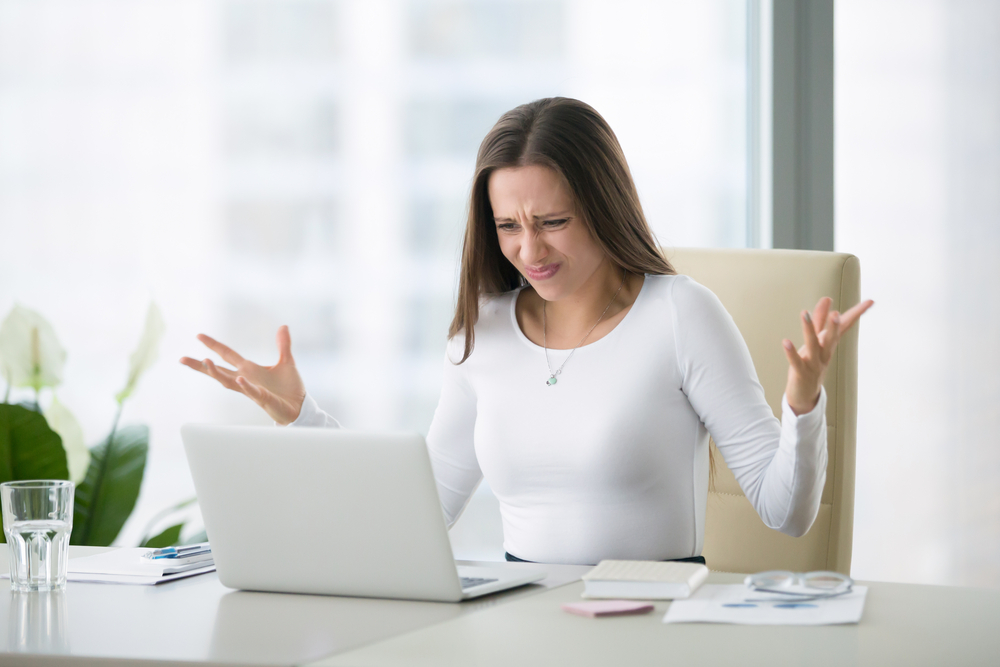 Frustrated loan officer at desk struggling with confusing mortgage software on her laptop