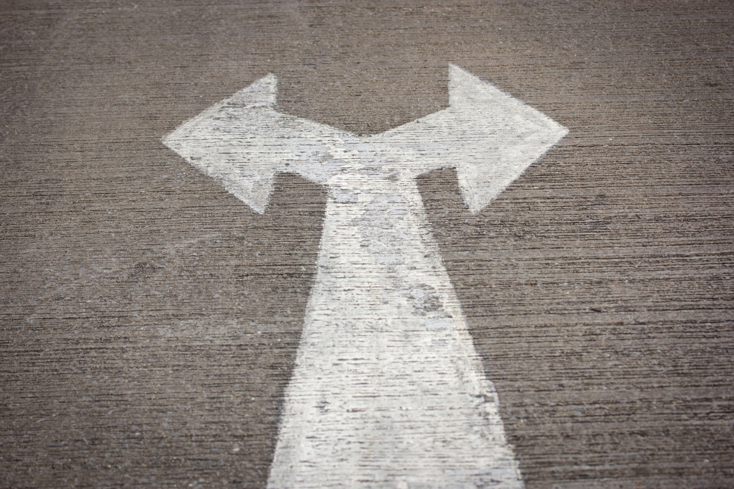 White arrow painted on pavement splitting into two directions, symbolizing decision-making between mortgage presentation software options.